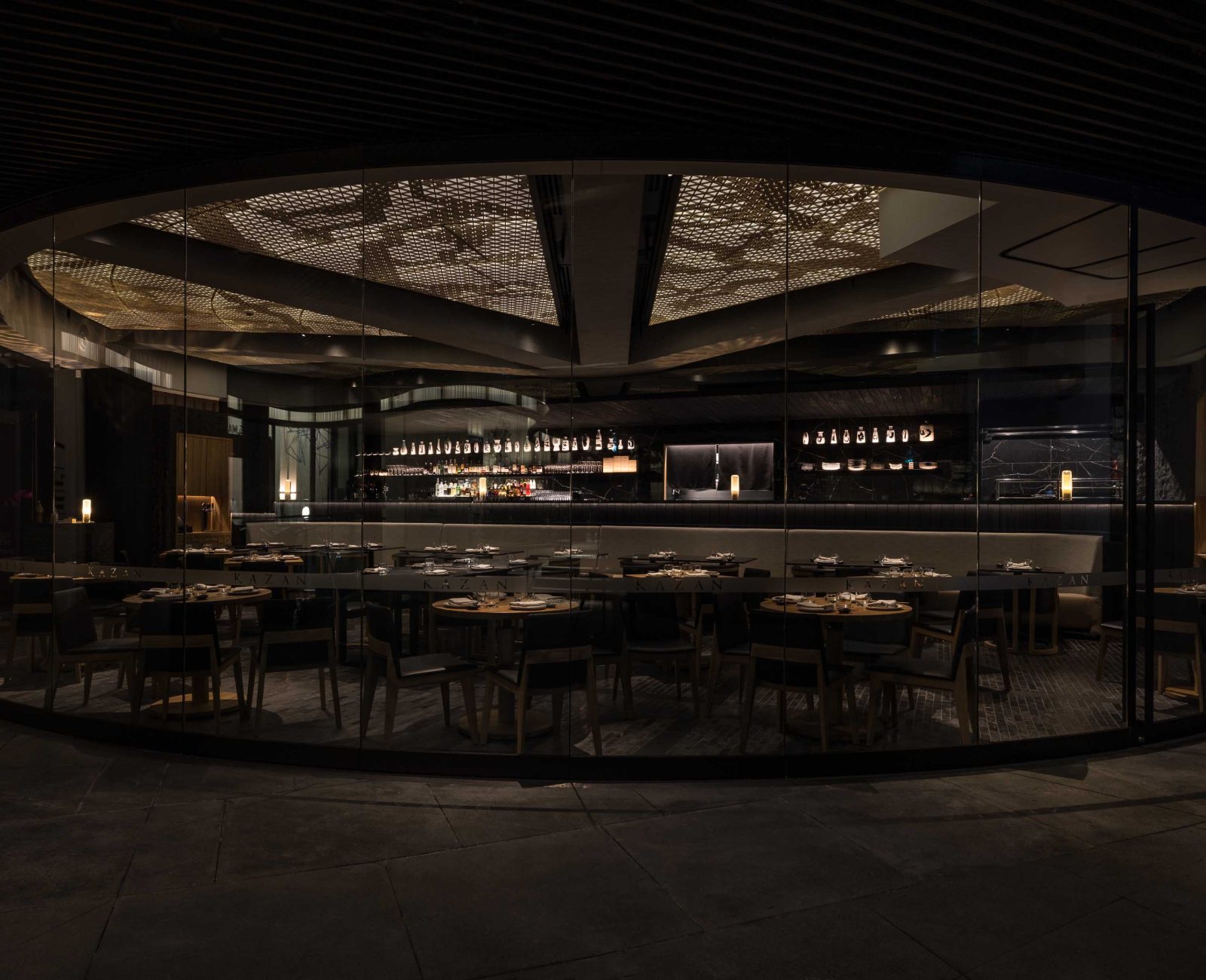 Elegant fine-dining room behind a curved glass wall, low amber lighting